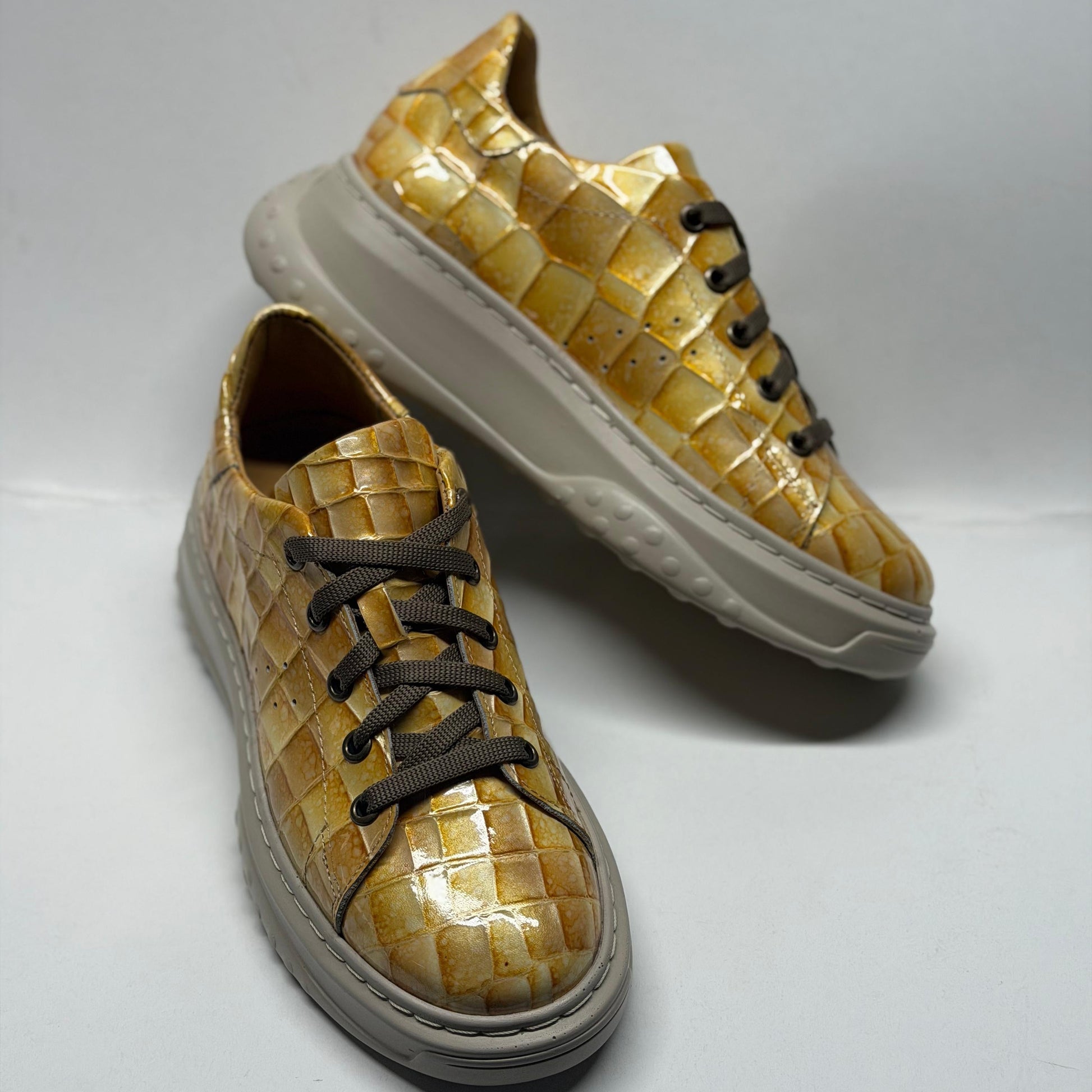 Pair of gold woven sneakers with white soles on a light gray background
