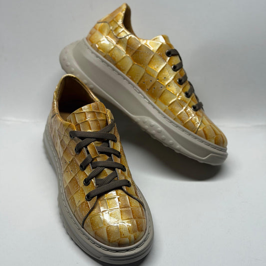 Pair of gold woven sneakers with white soles on a light gray background