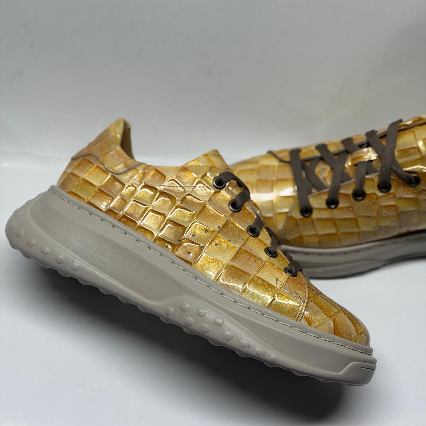 Gold woven sneakers with a white sole on a light gray background